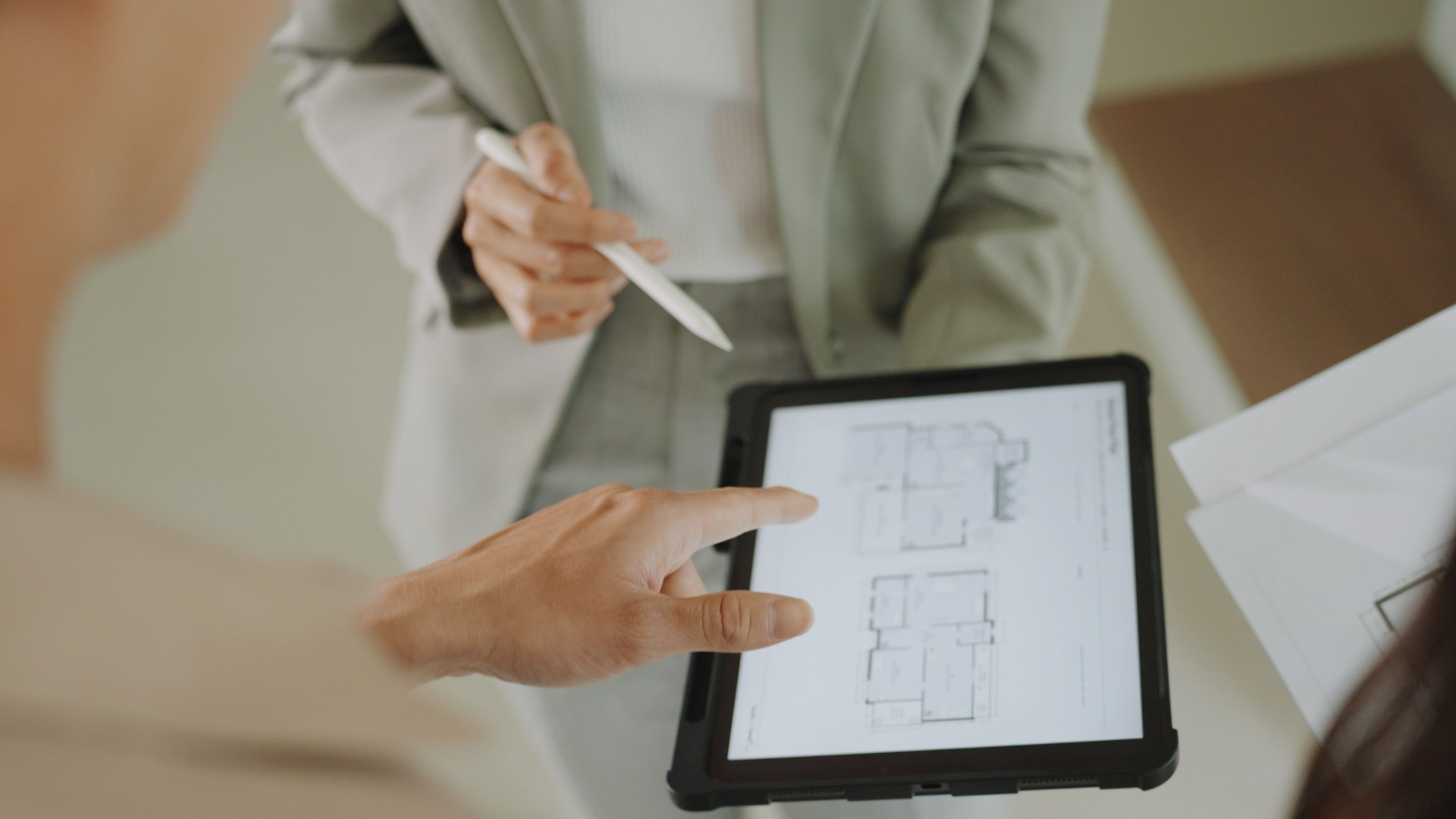 Close up of Real Estate Agent explaining floor plan house blueprint on a digital tablet to couple buying a property house